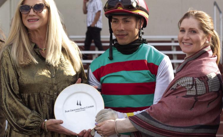 Five time Champion Jockey of the New Orleans Fairgrounds, Rosie Napravnik returned to the Winner's Circle for the 2025 season in her new vocation raising awareness of a program for retired racehorses. Pictured here with Jockey Jose Ortiz, Rosie presents the winners plate in honor of winning horse Montalcino.